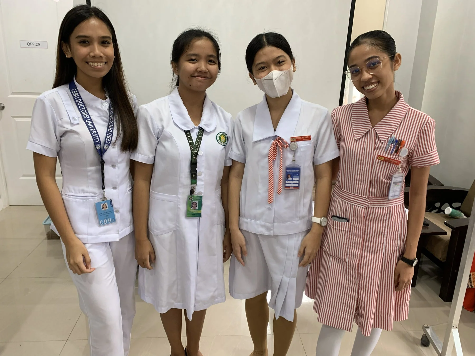 4人の若い女性が、医療系の制服と思われる服装で笑顔で並んで立っている写真。それぞれ異なる学校のIDカードを身につけている。