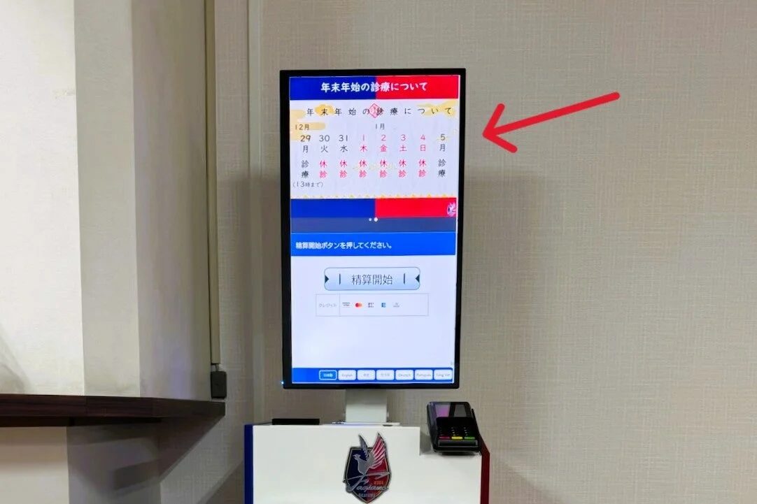 医療機関に設置された精算機が映されており、年末年始の診療スケジュールと支払い手続きの案内が表示されています。