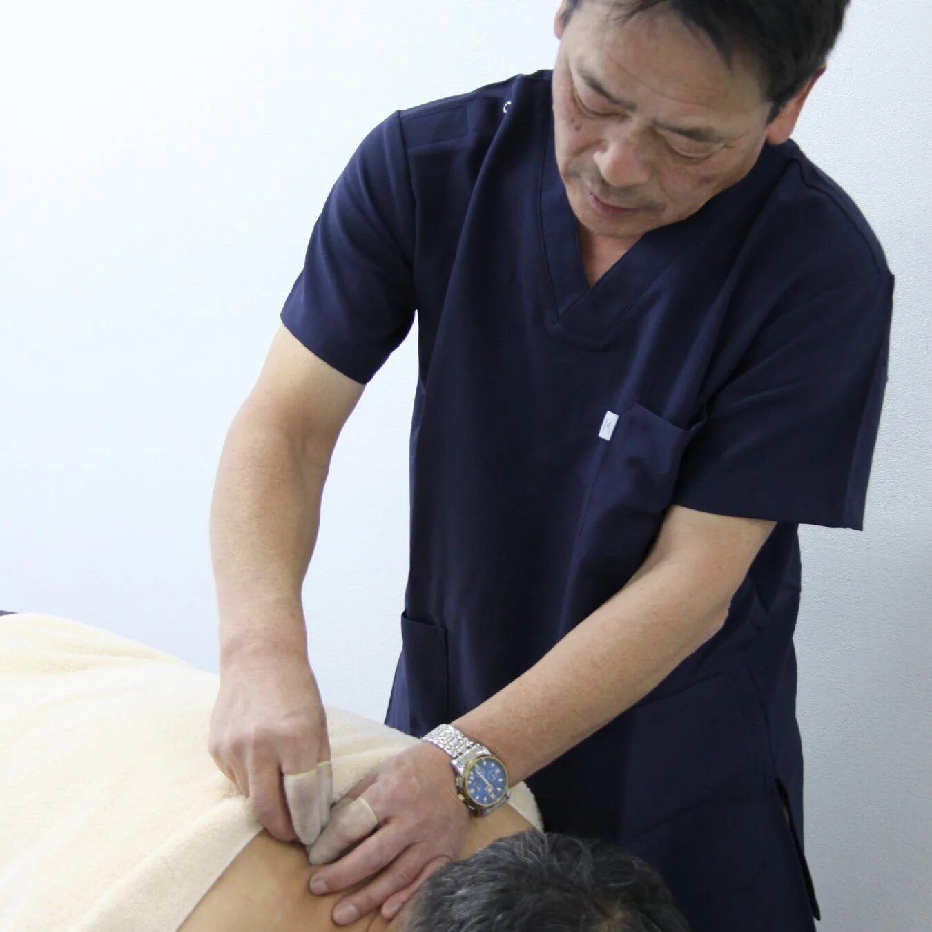 紺色の制服を着た施術者が患者の背中下部に手を当てて施術を行っている