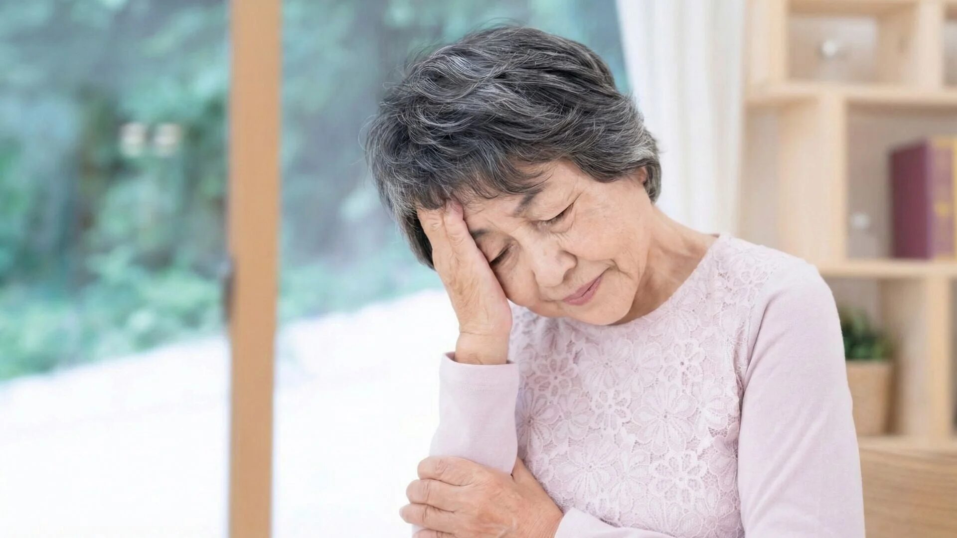 頭に手を当ててつらそうな高齢女性のクローズアップ