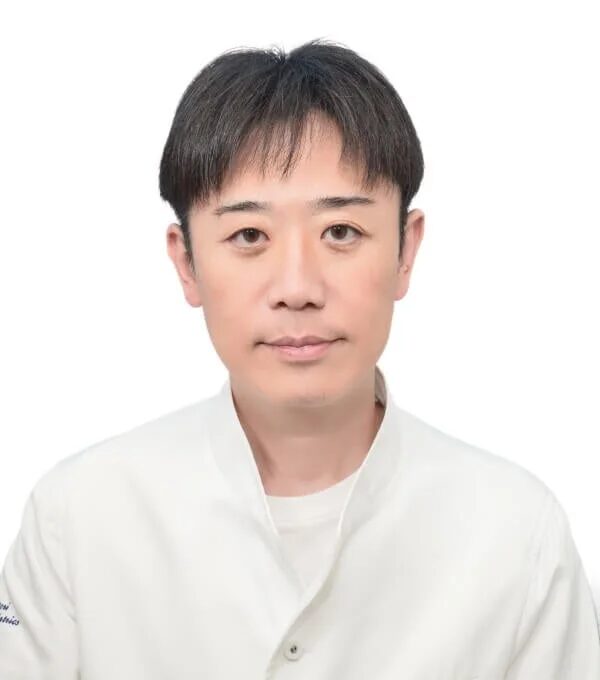 白い背景を背に、白衣を着用したアジア系の男性がカメラをまっすぐ見ているポートレート写真です。清潔感があり、真面目な印象を与えます。