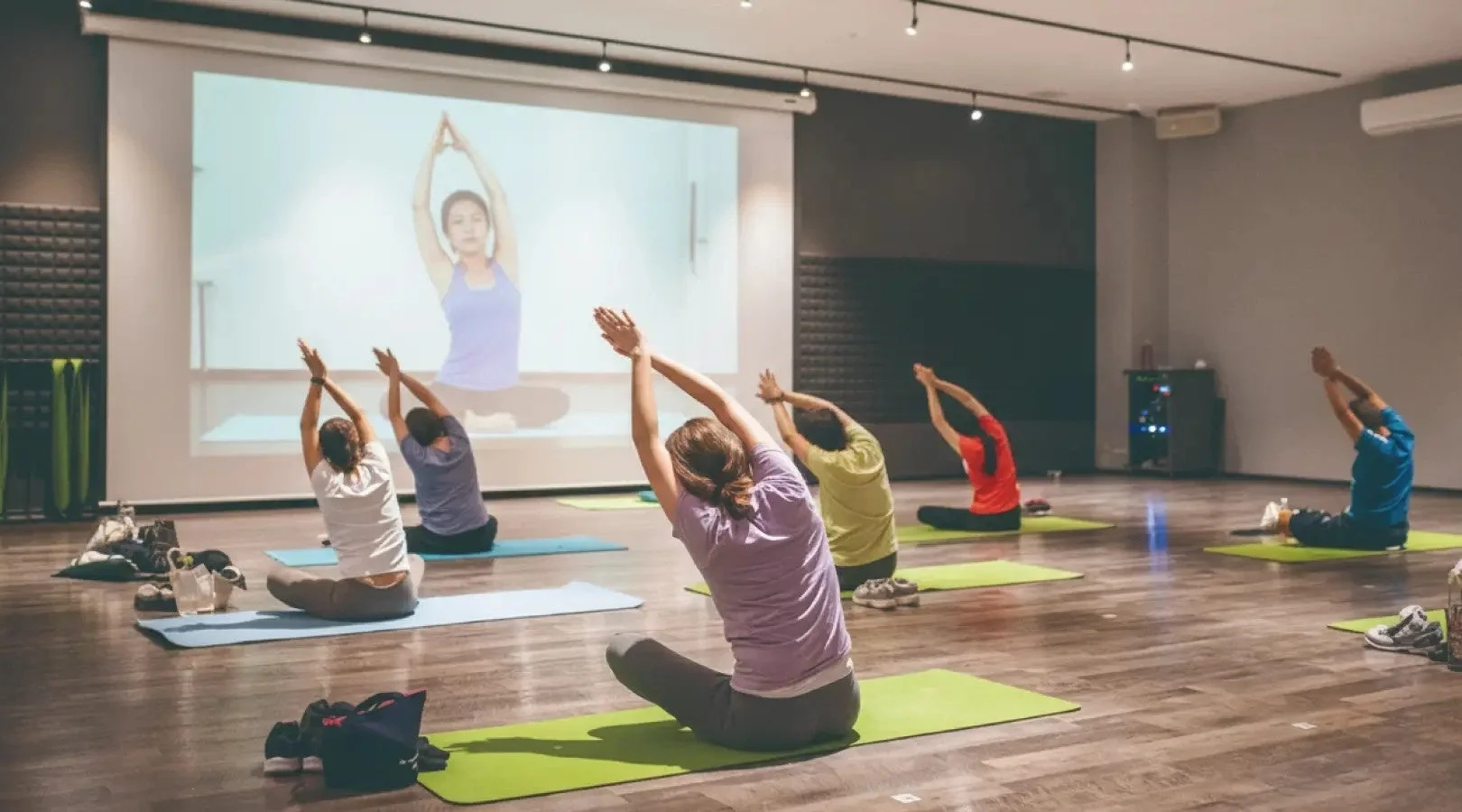 ヨガスタジオでプロジェクターに映し出されたインストラクターに合わせてヨガをする人々