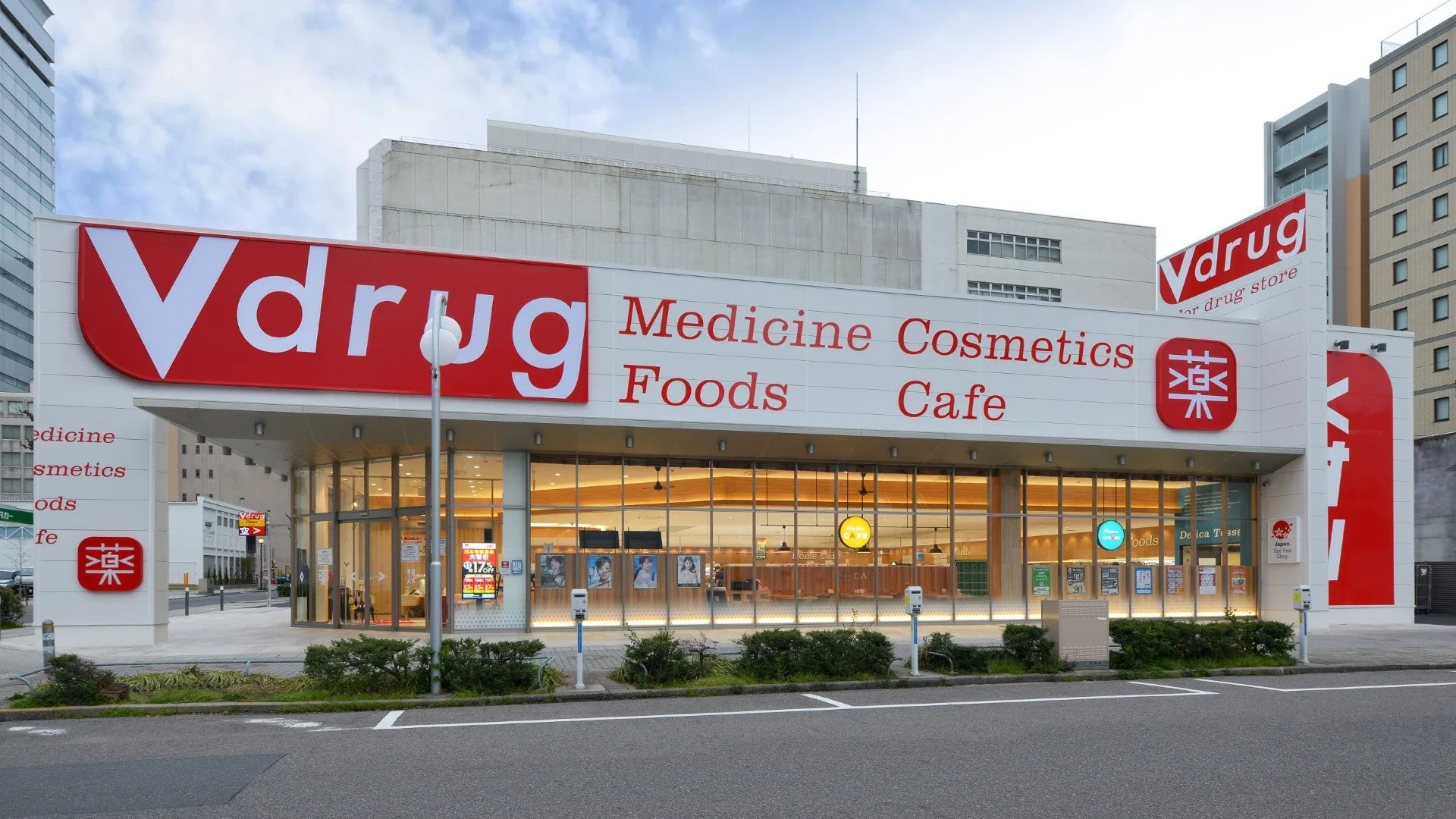 Vdrugドラッグストアの外観です。医薬品、化粧品、食品、カフェを扱う店舗で、「薬」の文字や「免税店」の表示が見られます。モダンなデザインで、広いガラス窓が特徴です。