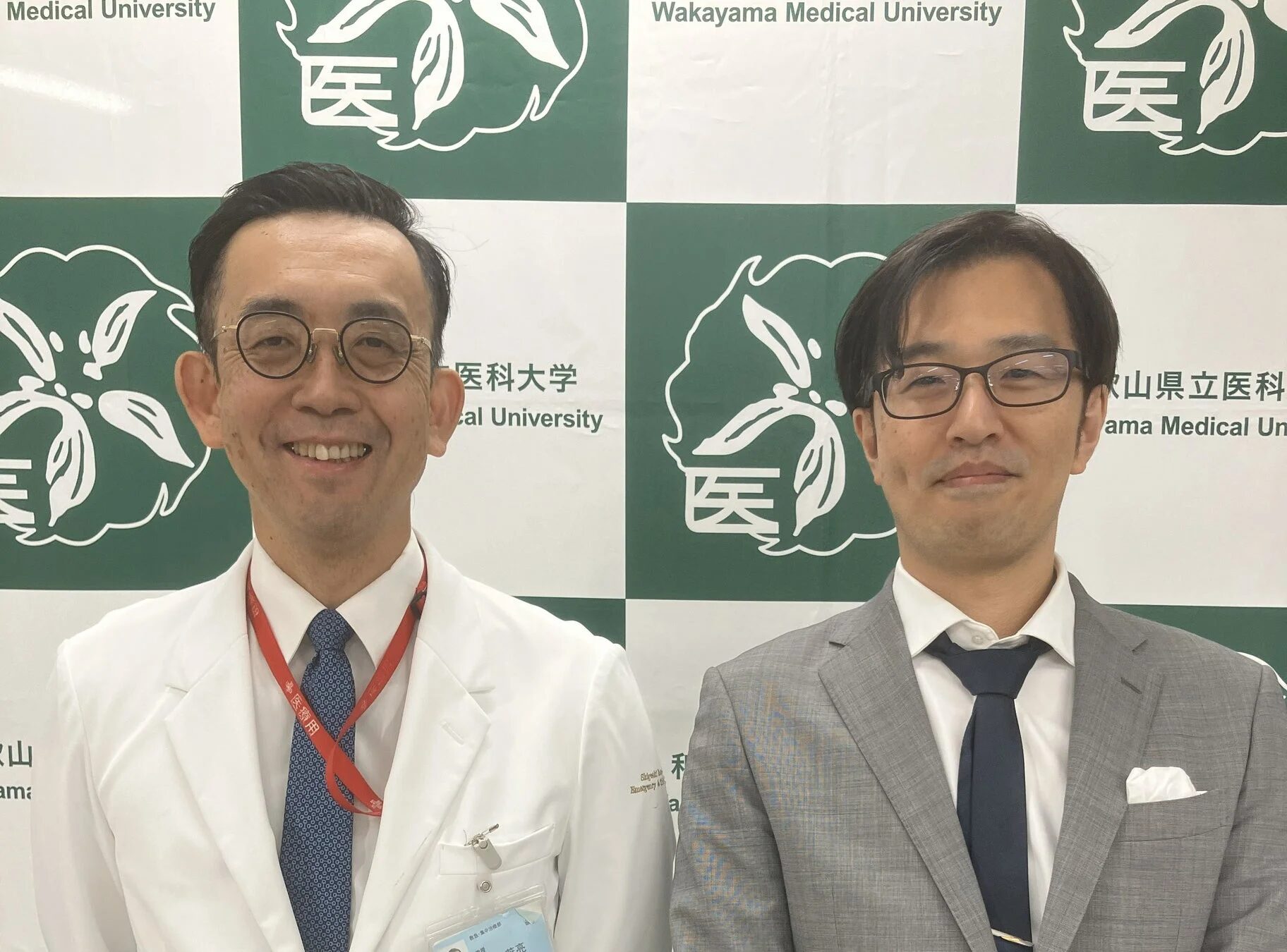 和歌山県立医科大学のロゴを背景に並ぶ二人の男性