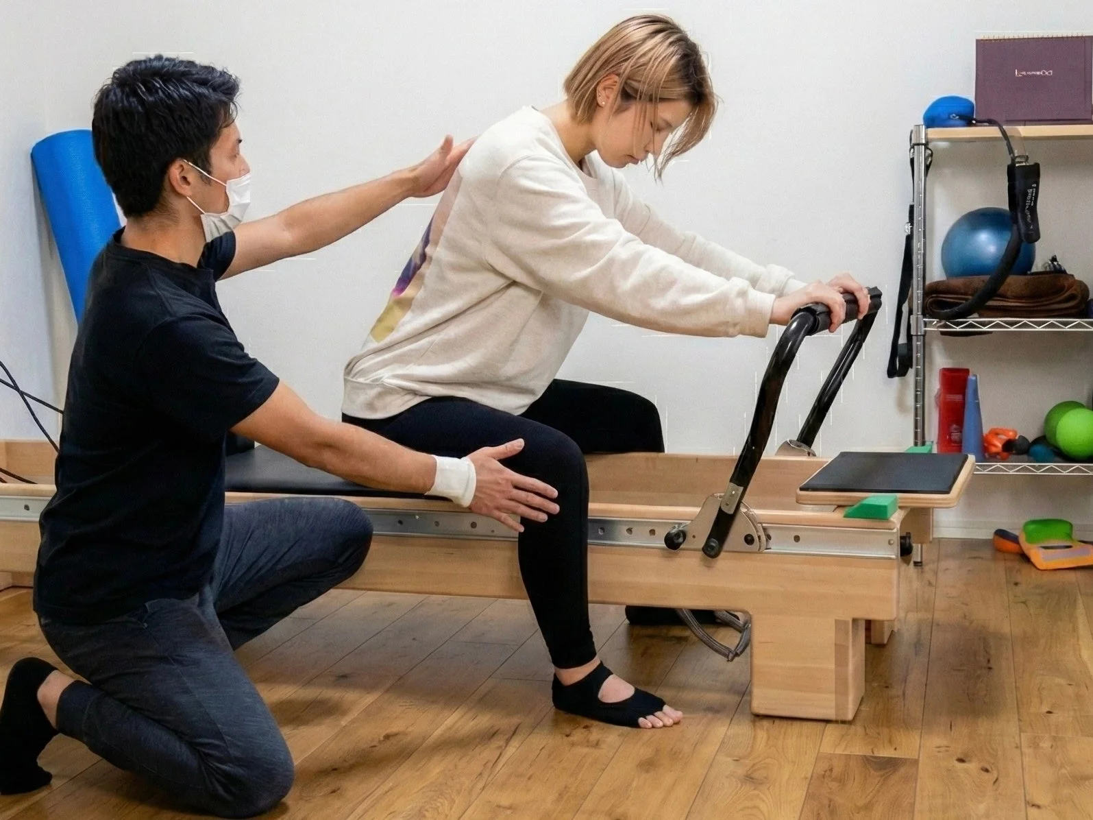 ピラティススタジオで、トレーナーが女性のクライアントにリフォーマーを使ったエクササイズを指導している様子