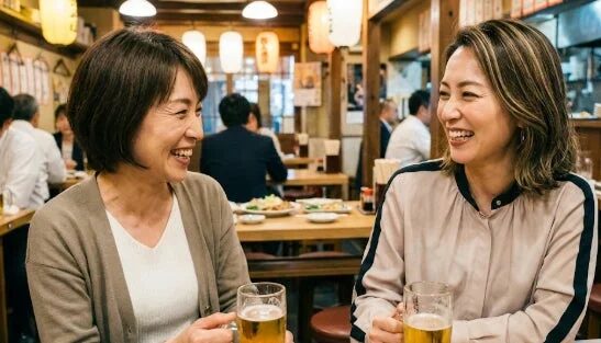居酒屋でビールを片手に笑顔で会話を楽しむ二人の女性。和やかな雰囲気の中で、食事と友情を深めている様子が伺えます。