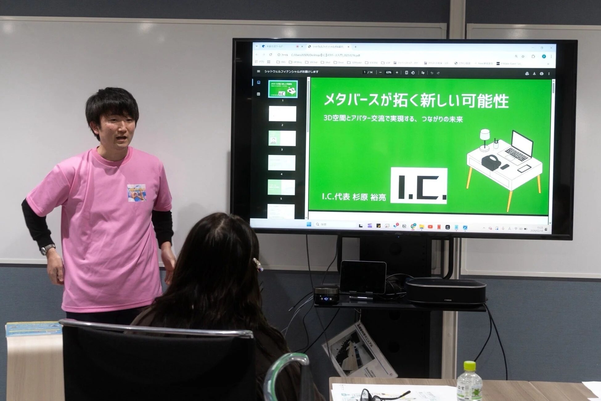 プレゼンテーションを行うピンクのTシャツを着た男性