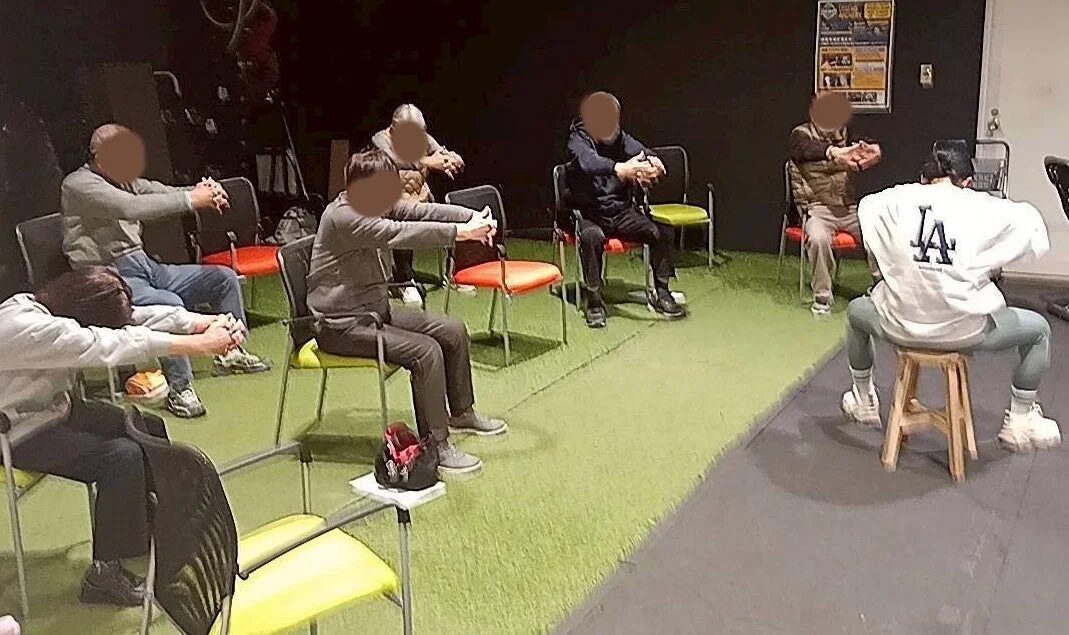 屋内で数人の人々が椅子に座ってグループで運動やストレッチを行っている様子