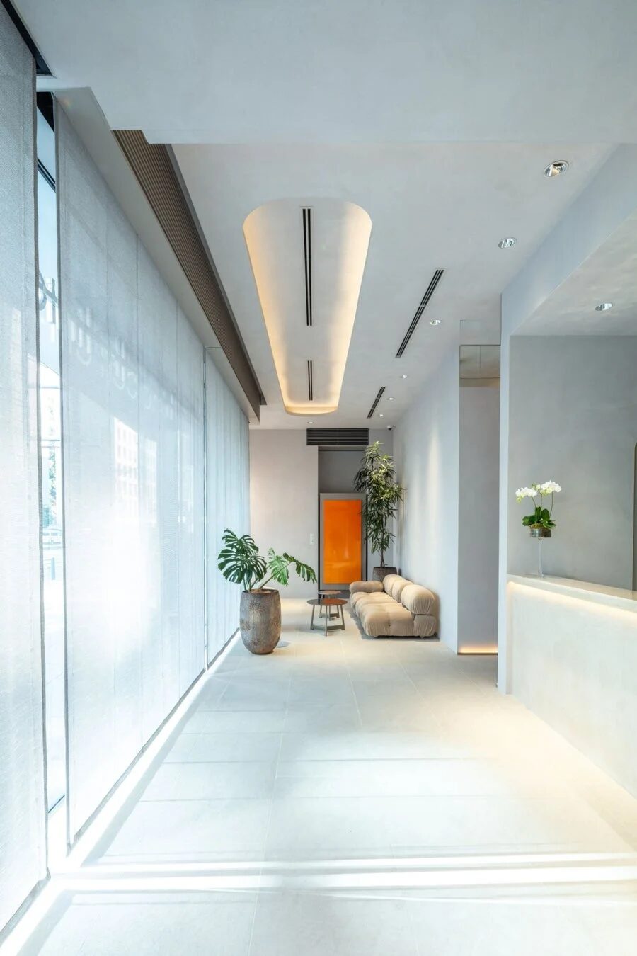 モダンインテリア、ロビー、待合室、ミニマリスト、ホテル、オフィス、間接照明、観葉植物、白い空間、ベージュソファ、オレンジドア、受付