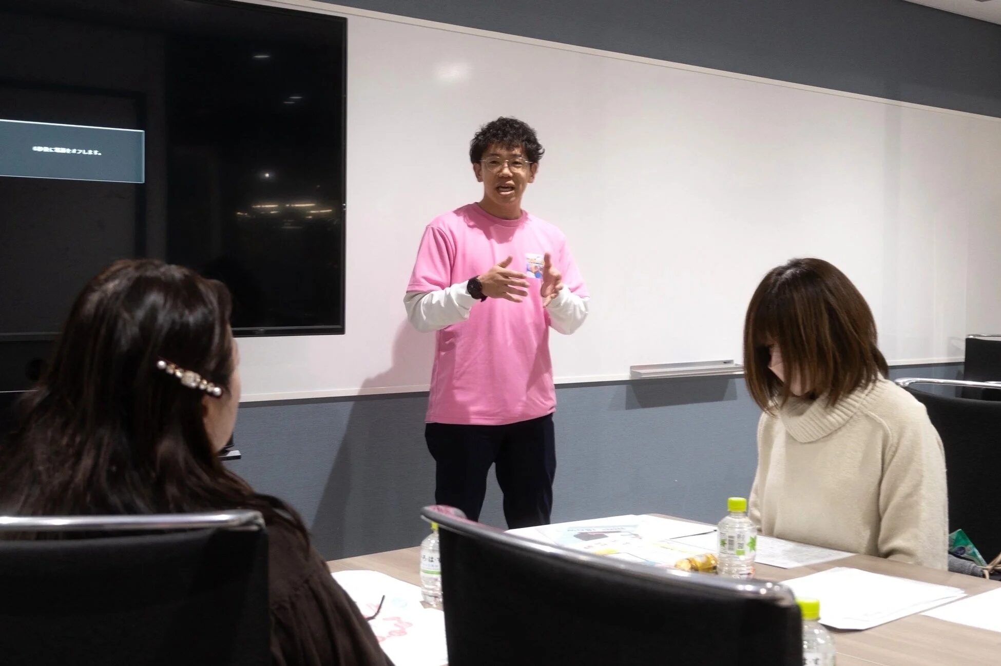 会議室でプレゼンテーションを行う男性と、話を聞く女性たち