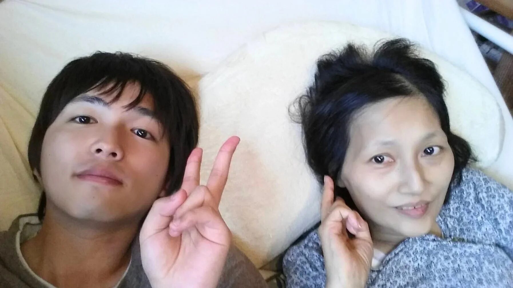 若者がベッドに横たわり、ピースサインをしている自撮り写真