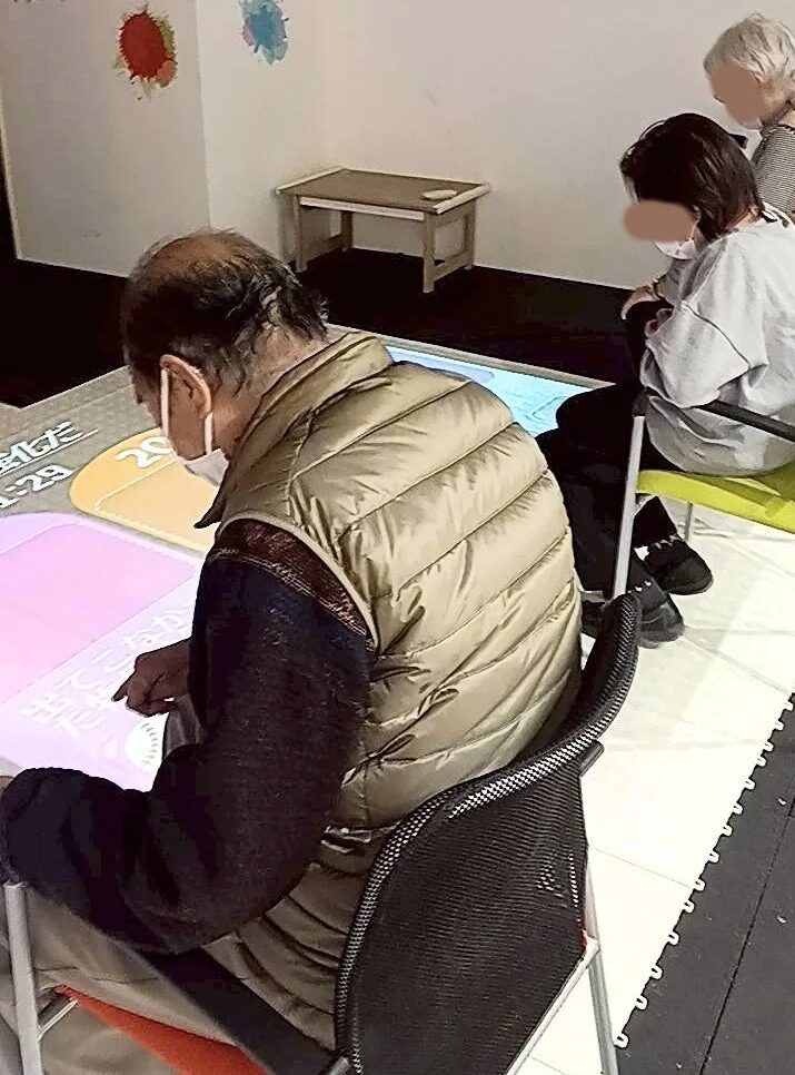 高齢者がマスクを着用し、インタラクティブなデジタルテーブルを操作している様子