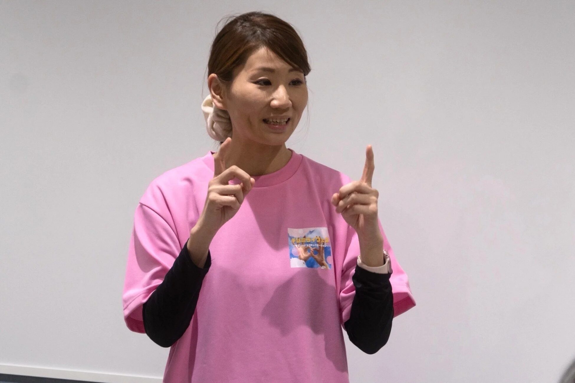 ピンクのTシャツを着て手話で話す女性