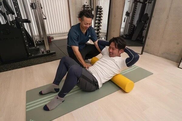 ジムでフォームローラーを使った運動をサポートするトレーナー