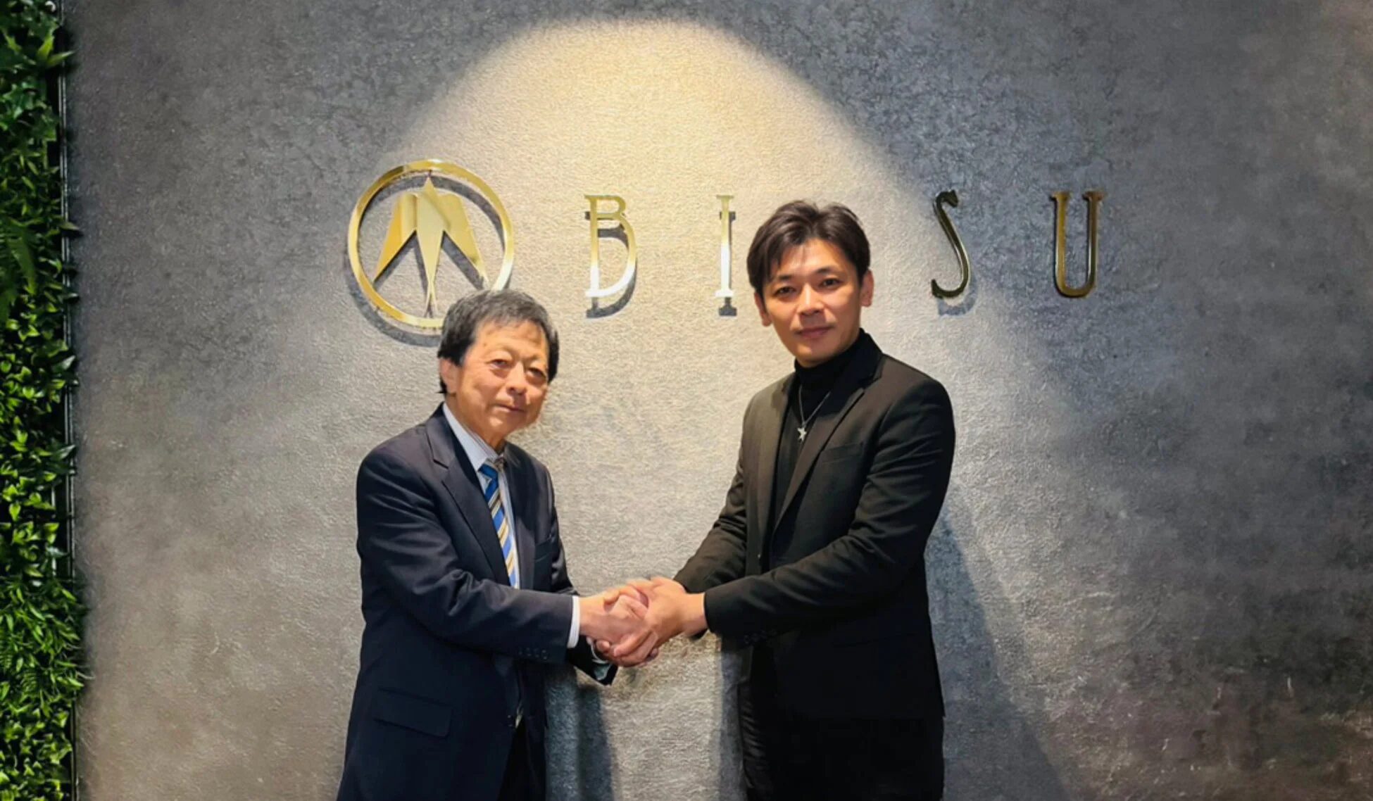 ビジネススーツを着た2人の男性が、企業ロゴ「BISU」の前で握手を交わしている