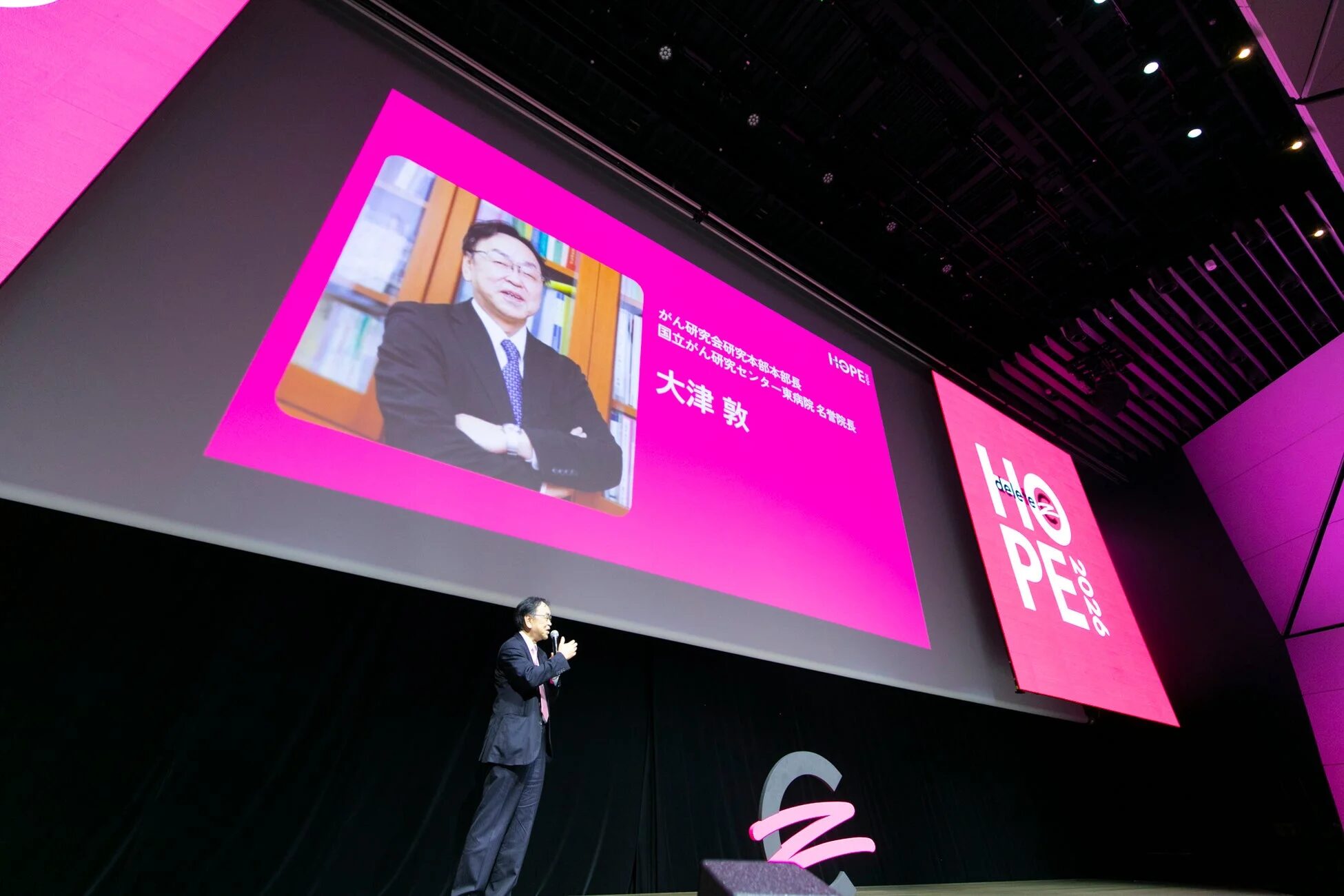 イベントで講演する大津敦氏。背後のスクリーンには「がん研究会研究本部部長 国立がん研究センター東病院名誉院長 大津 敦」と表示されています。
