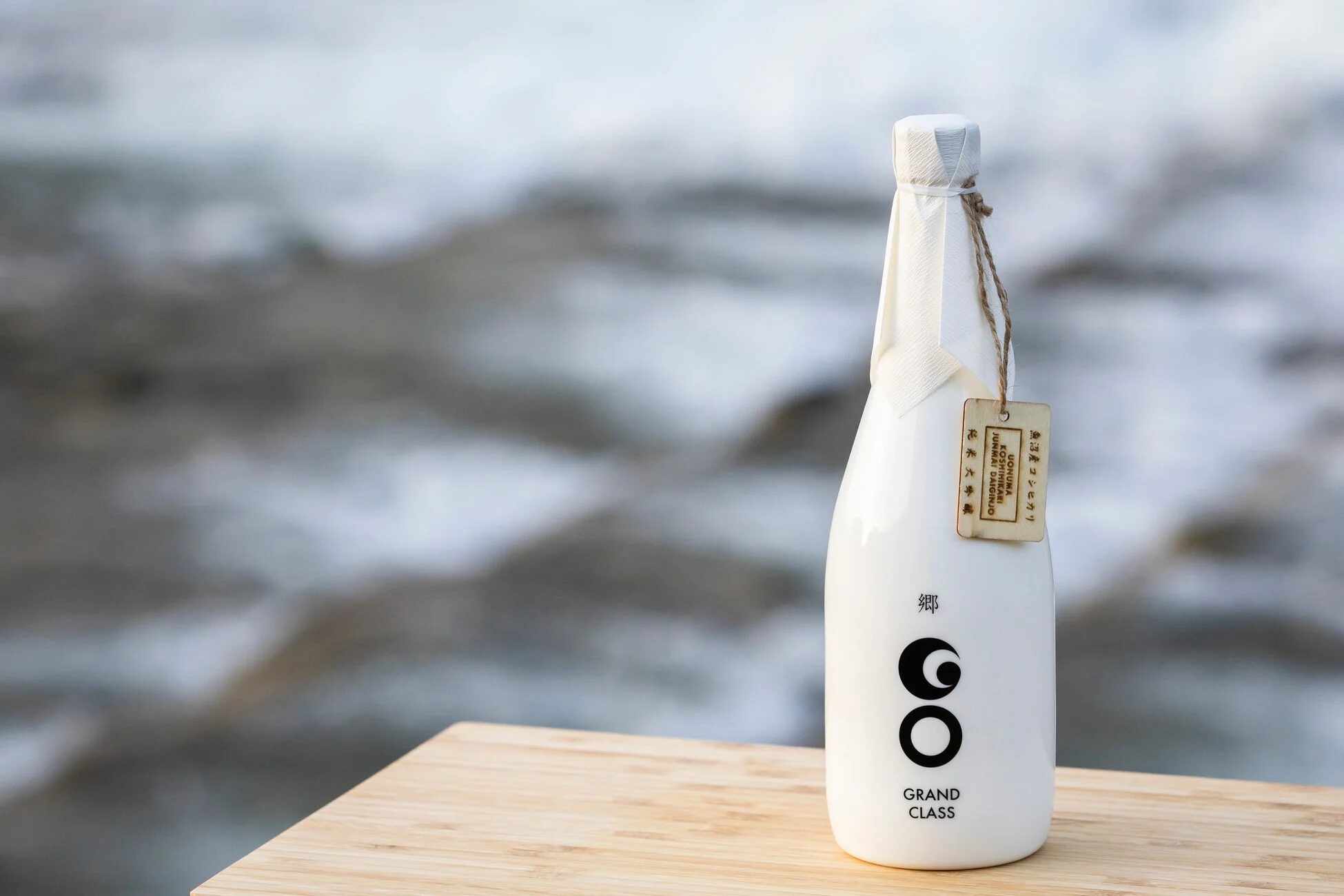 木製の台に置かれた、白いボトルに入った日本酒「郷 GRAND CLASS」。