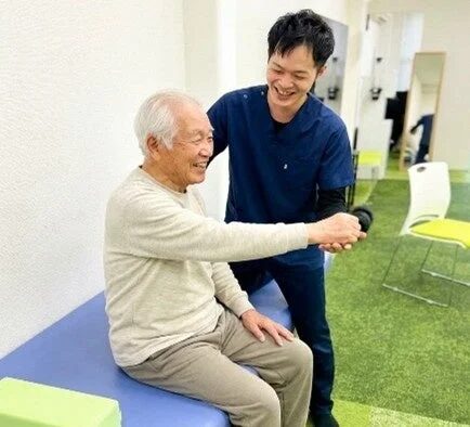 笑顔の高齢男性が理学療法士のサポートを受けながら運動している様子