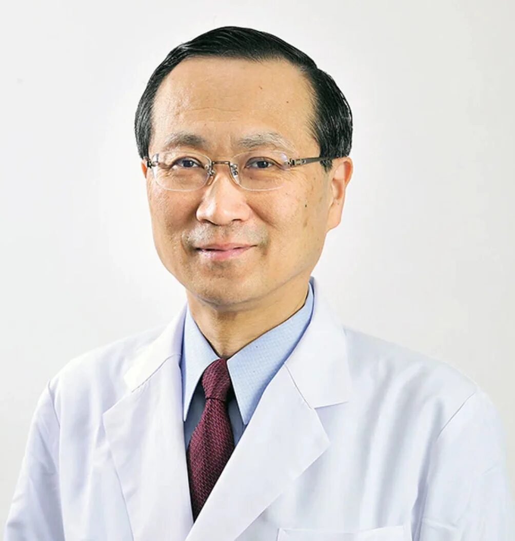 白衣を着て眼鏡をかけたアジア系の男性医師のポートレートです。穏やかな笑顔でカメラを見つめており、専門的な雰囲気を醸し出しています。