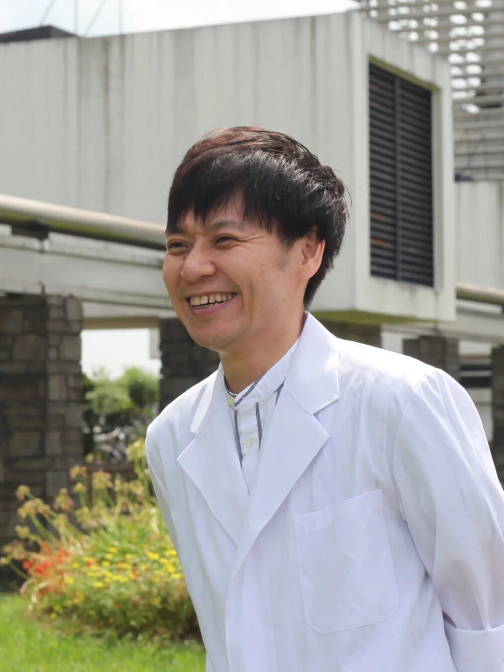 屋外で白い白衣を着た男性が、満面の笑みを浮かべています