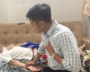 男性がソファに横たわる人の脈拍を測る様子