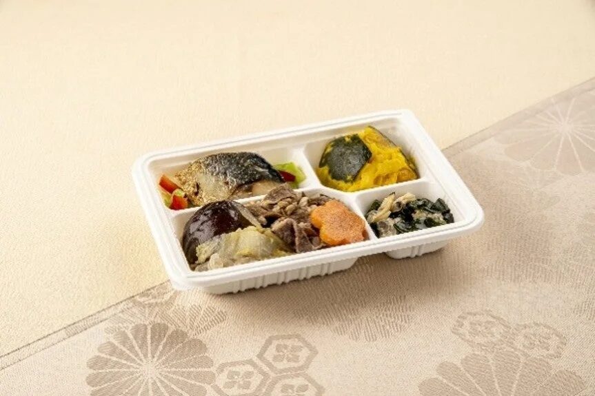 焼魚、かぼちゃの煮物、肉と野菜の煮物などが入った、仕切りのある白いお弁当箱が写っています。様々な種類の和食のおかずがバランス良く詰められています。