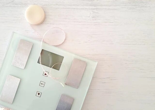 白い木目調の背景に、デジタル体重計とメジャーが置かれています。健康やダイエット、体の測定を連想させる清潔感のあるイメージです。